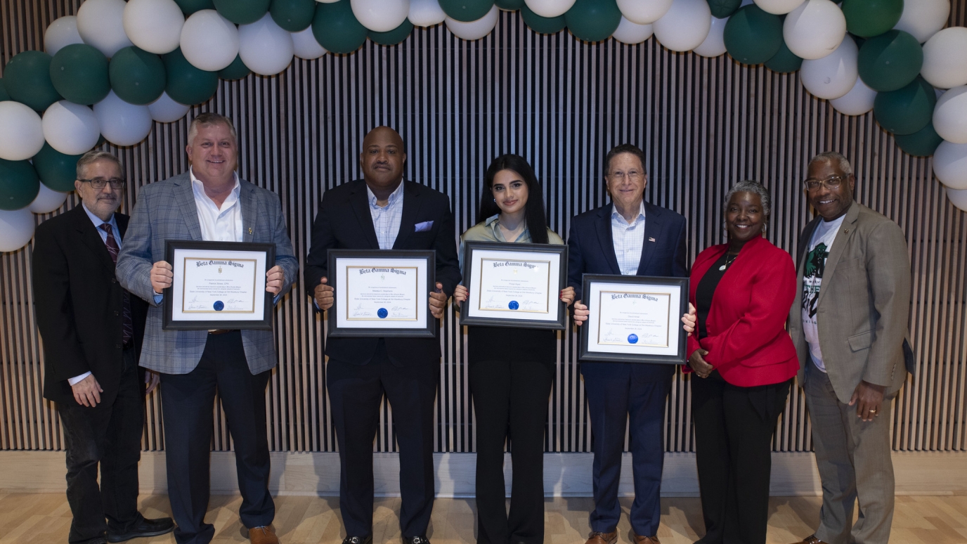 Four awardees holding certificates are congratulated by three campus officials