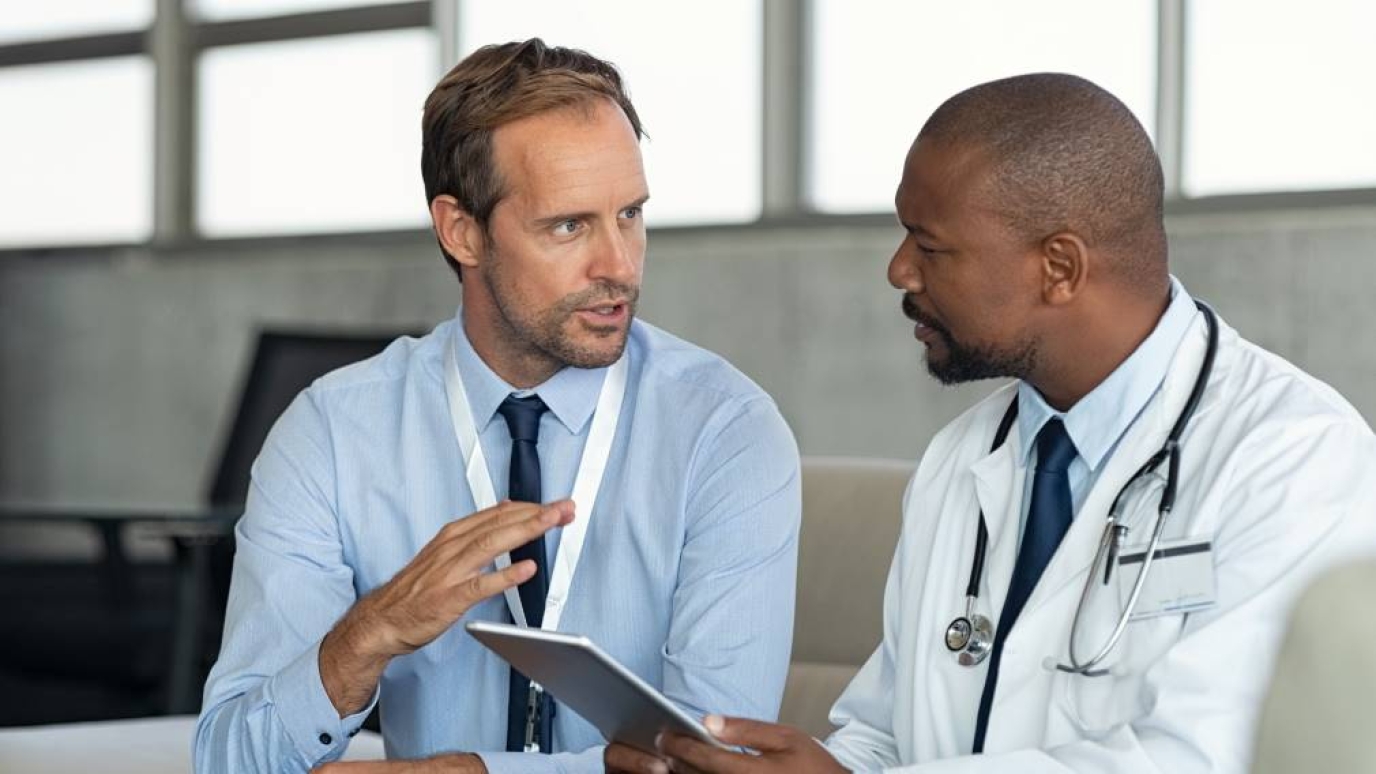 Man in professional dress speaks with man in doctor's garb