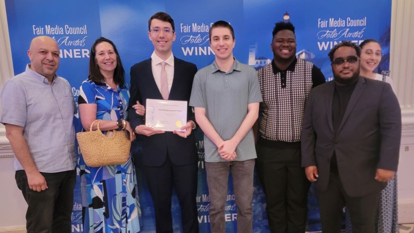 Group of seven men and women with one young man holding an award certificate