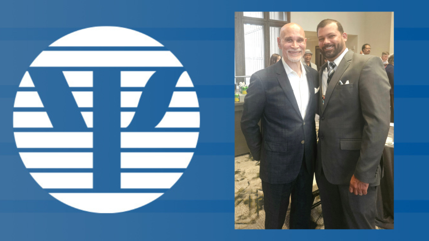 Two adult men in business dress against a backdrop of blue featuring a logo whereby a blue y appears within a white circle