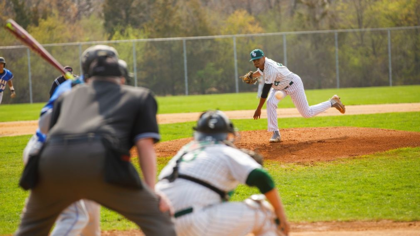 Baseball pitcher hurls pitch to batter while umpire awaits the action