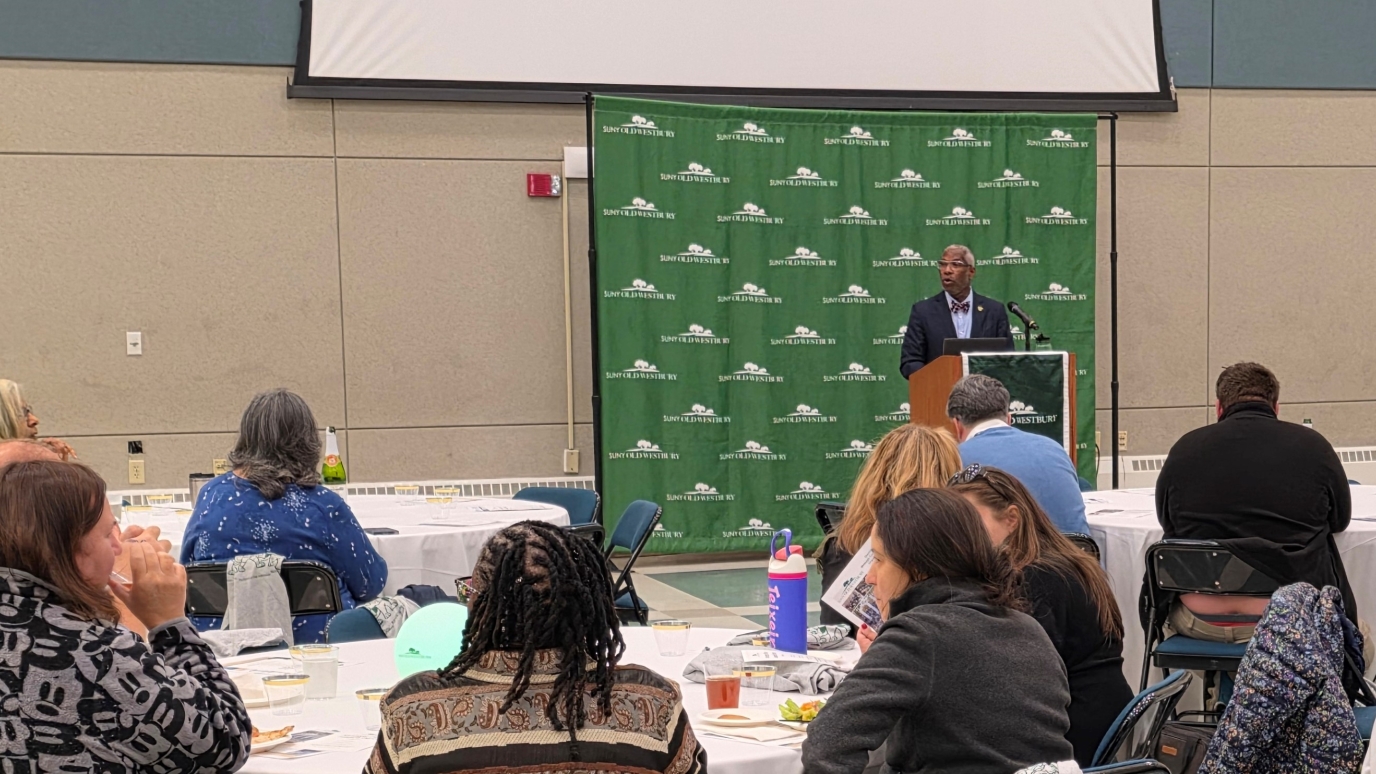 AFrican American man at a podium speaking before a large crowd