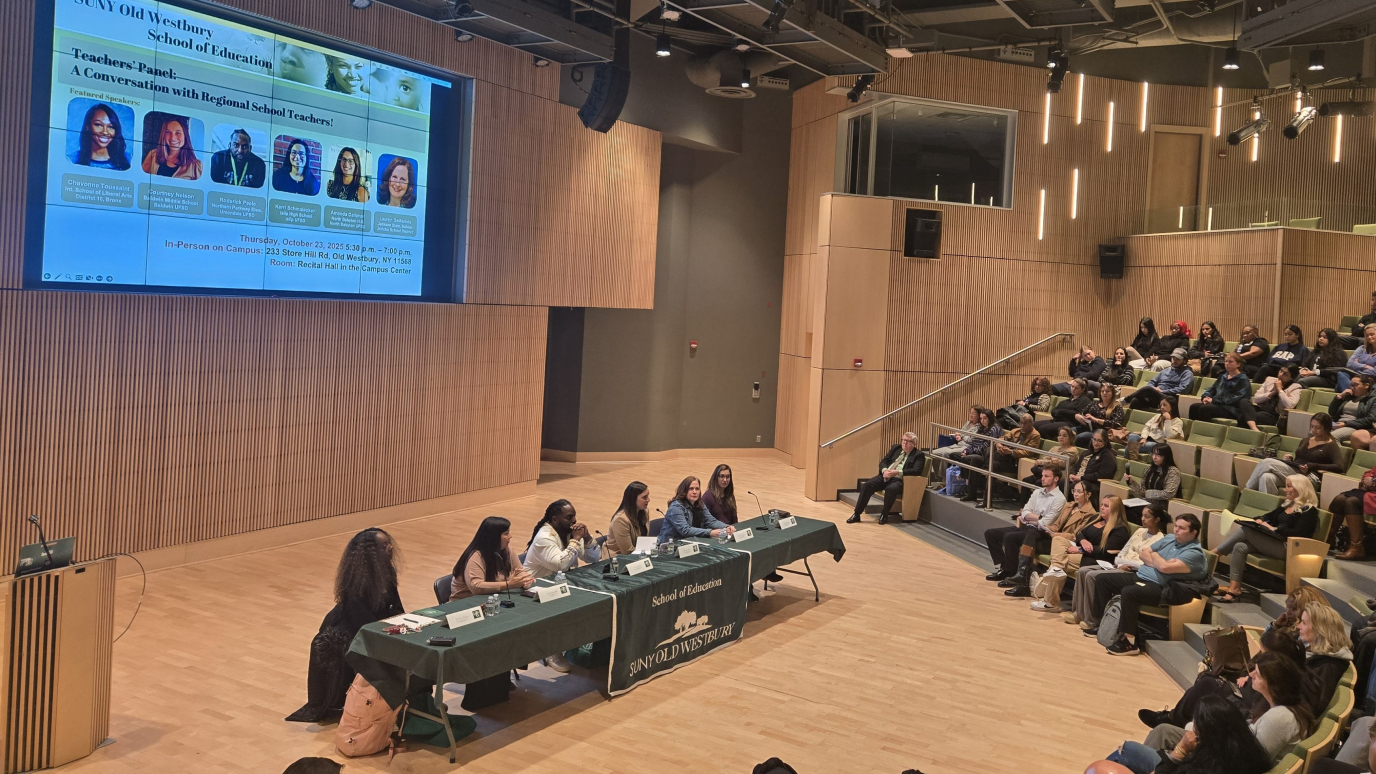 Panelist on stage in recital hall with audience seated before them.