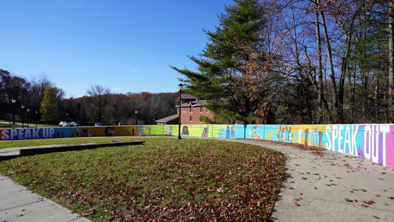 Wall featuring multicolored paintings of diverse young people and words including speak up and speak out