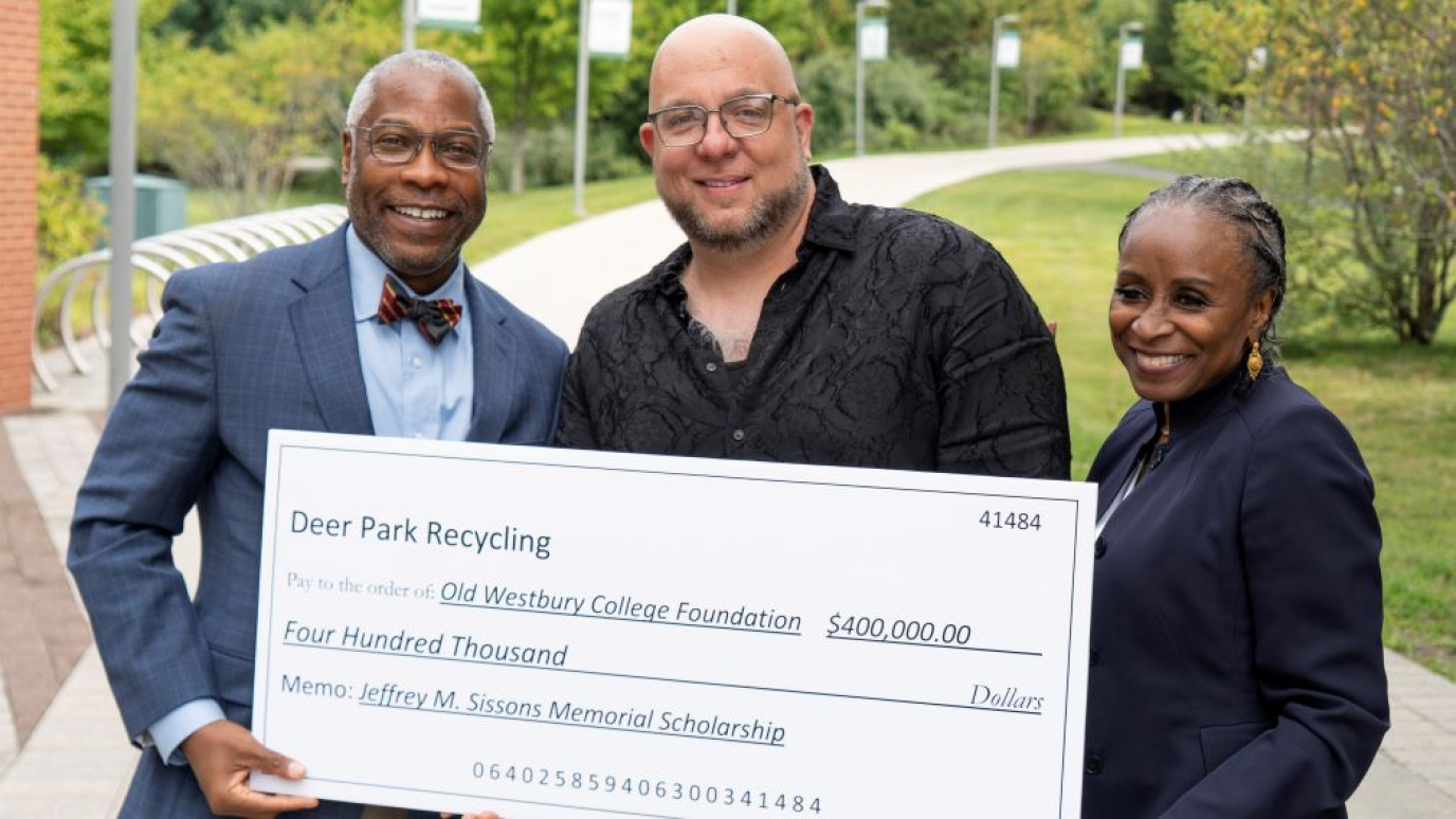 African American man and African American woman accept a mock-up donation check from Caucasian man