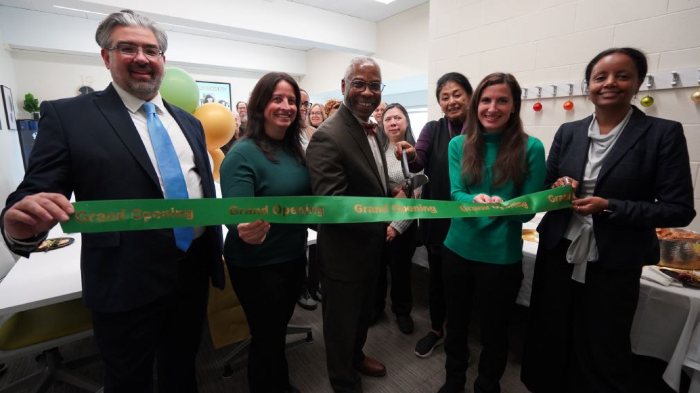 Six men and women in professional attire cut a large green ribbon