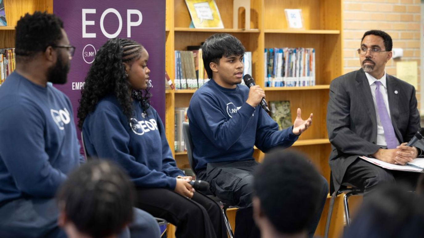 Hispanic young male speaks into a microphone as three others look on