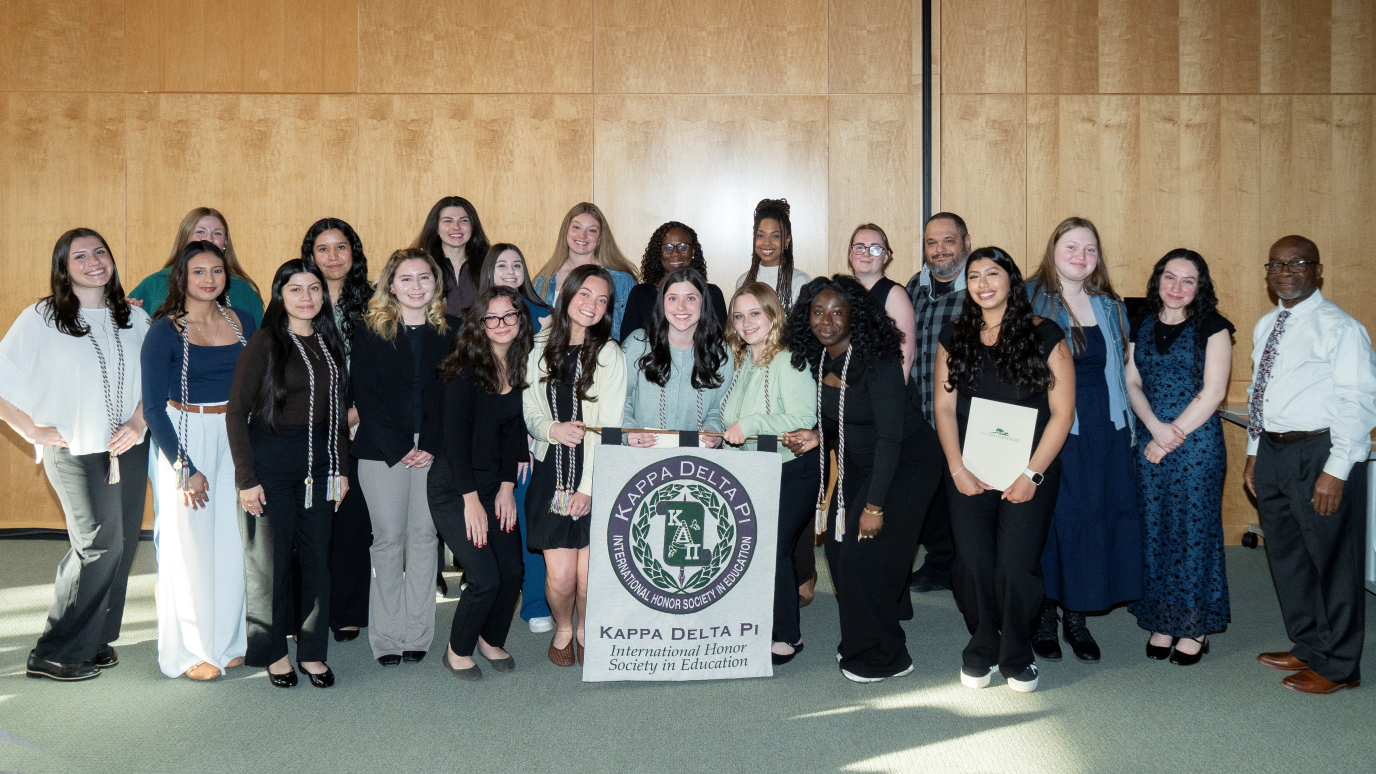Diverse group of 20 women and two men pose for a group photo with a black and white Kappa Delta Phi banner