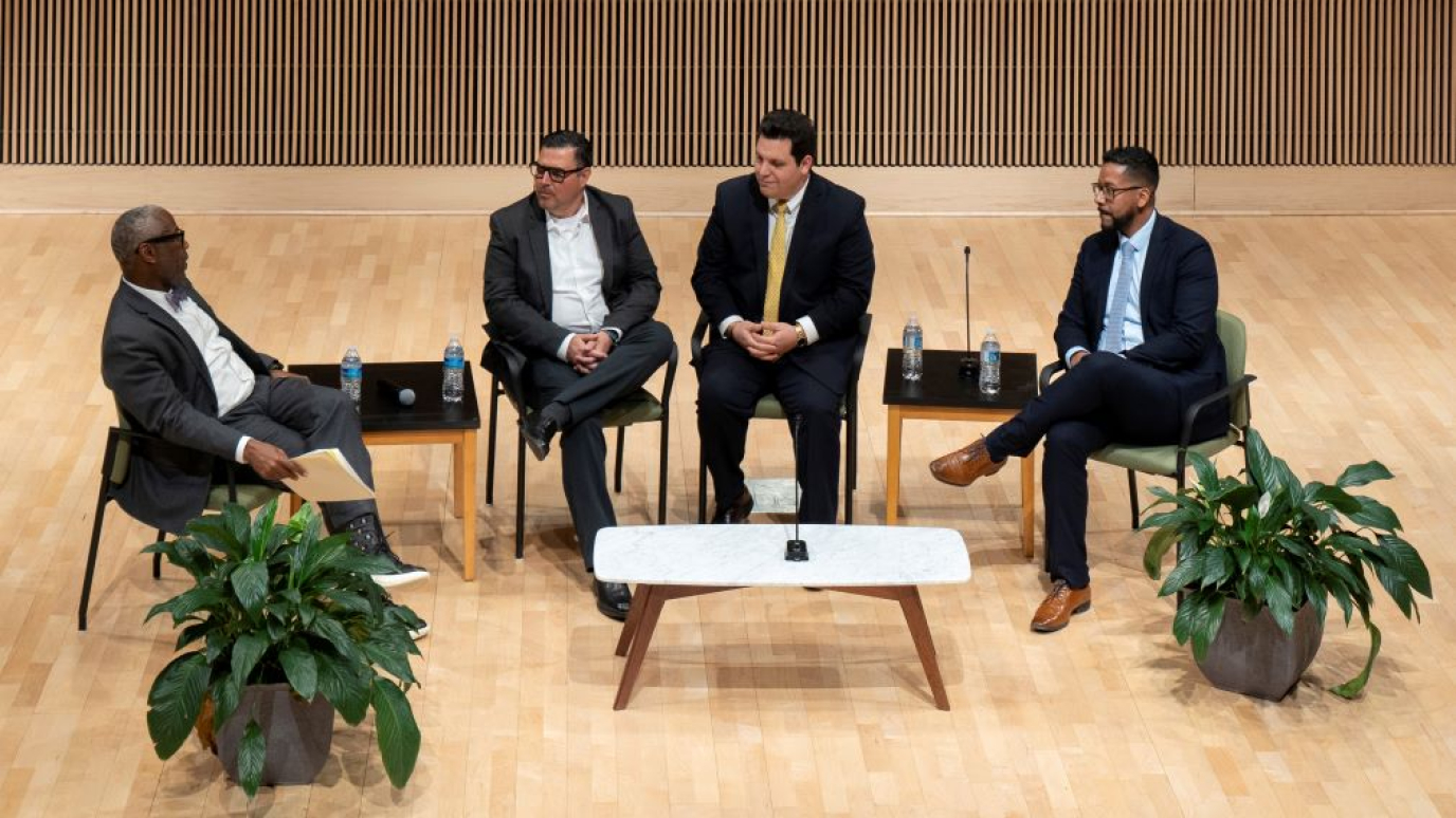 Four men in professional dress seated on a stage and in conversation