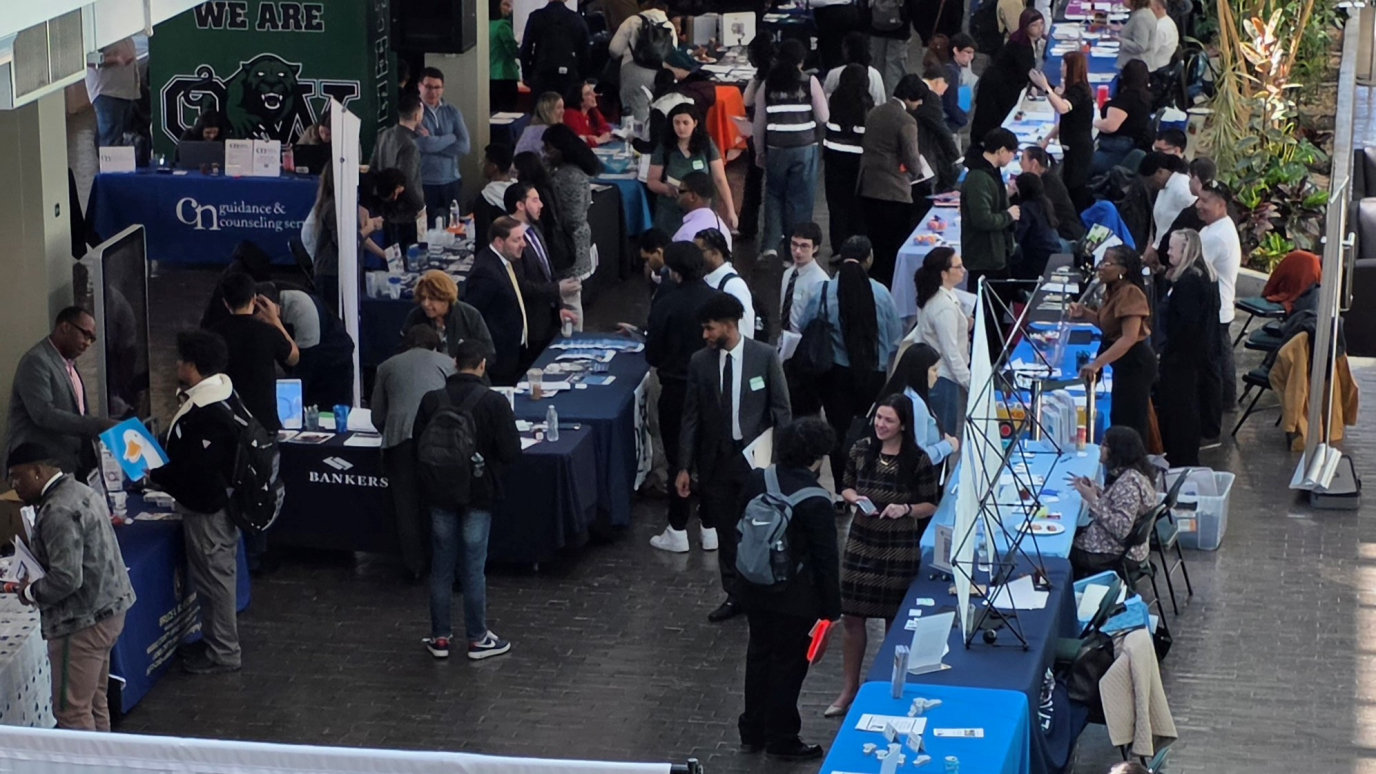 Large group of students in an atrium filled with tables manned by professionally dressed men and women