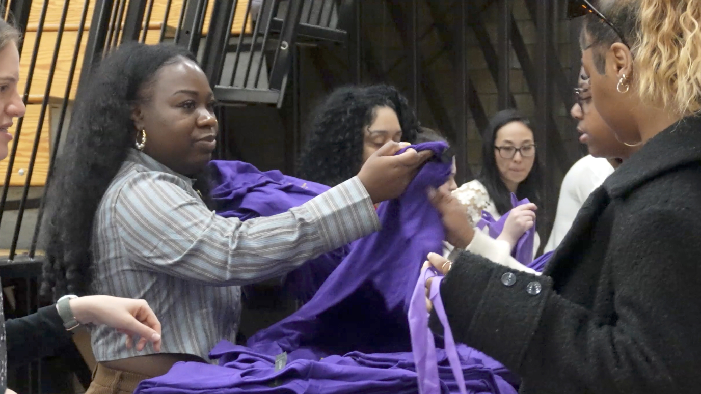 Three women in professional attire hand out tee shirts to students