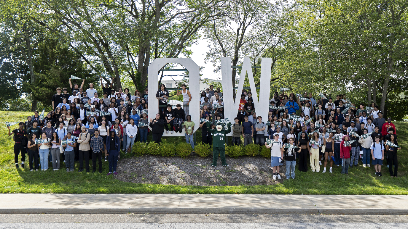 Large group of students standing outside around big O W white sign with green panther mascot.
