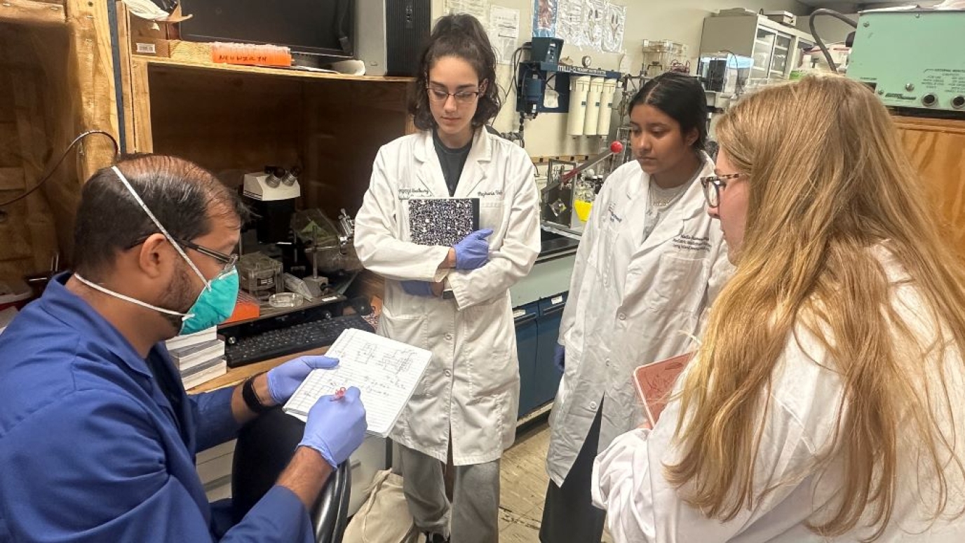 Three young ladies in lab coats work with a professor in a science research lab