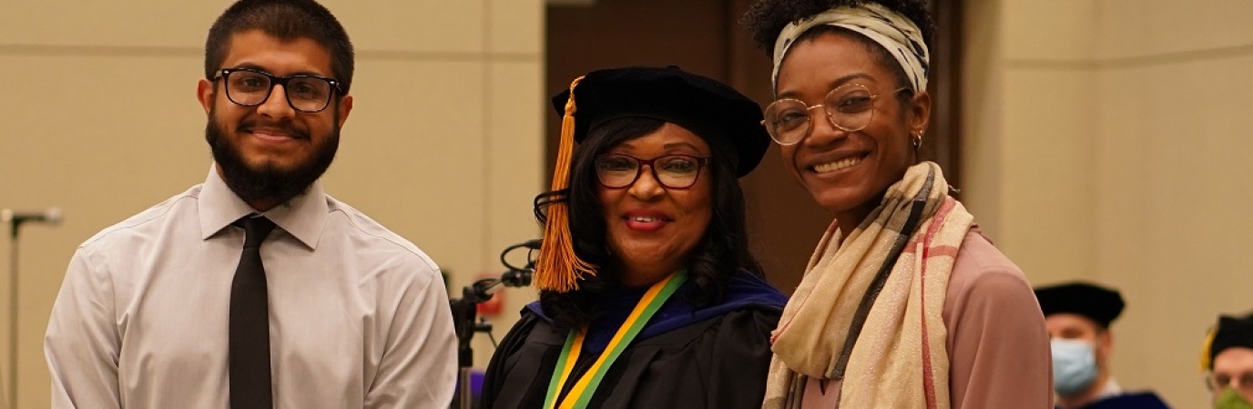 Two students with flanking an administrator in academic regalia