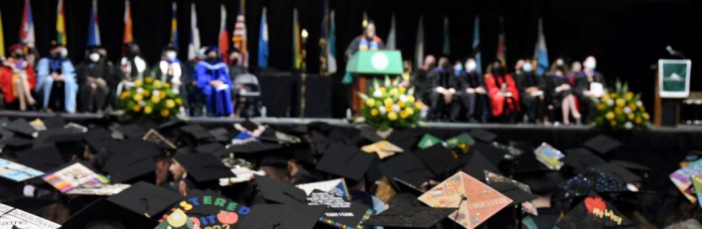 View from the audience of the overlooking approximately 50 graduates with decorated mortarboards