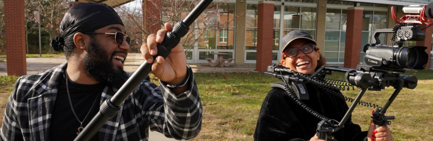 Two students using a video camera and boom microphone outside the NAB 