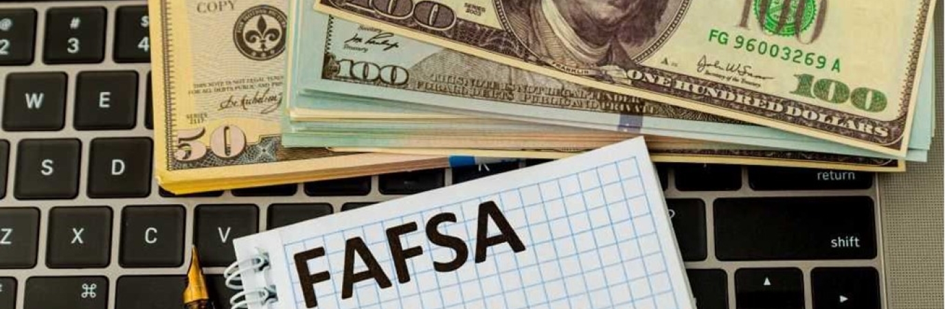 A FAFSA form on top of a keyboard with 100 dollar bills stacked on the keyboard also