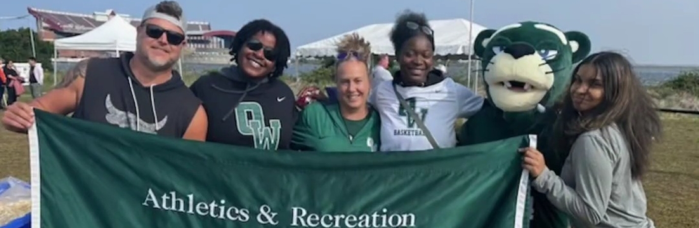 Four athletes and coaches stand with mascot OWWIN holding a campus banner