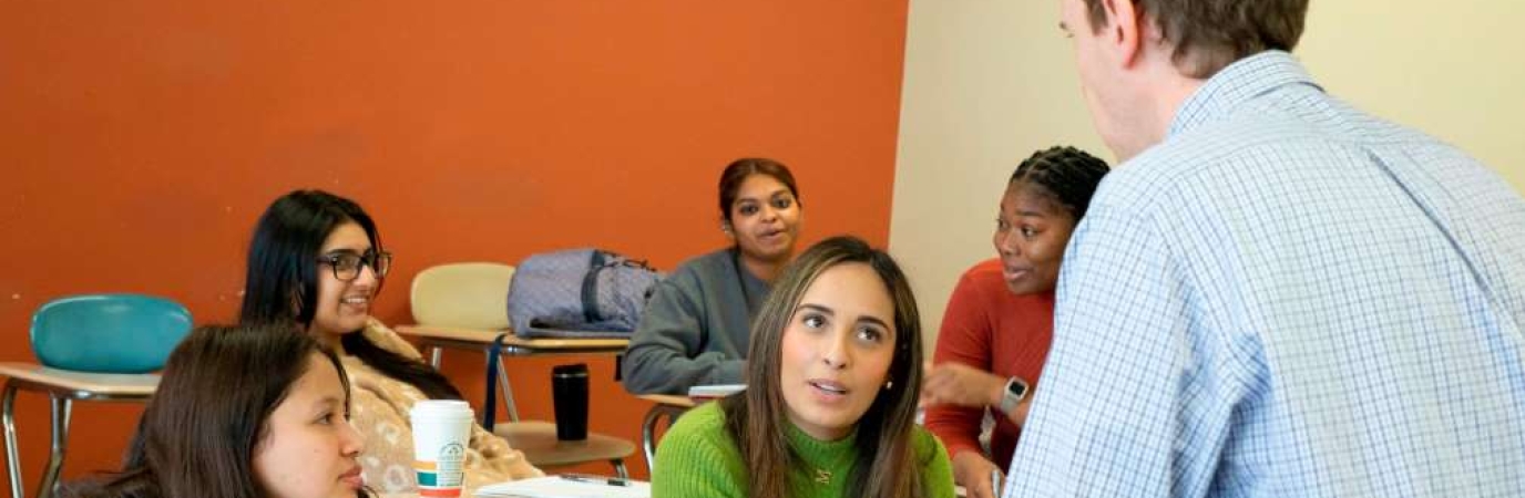 Faculty member standing while speaking with three seated students