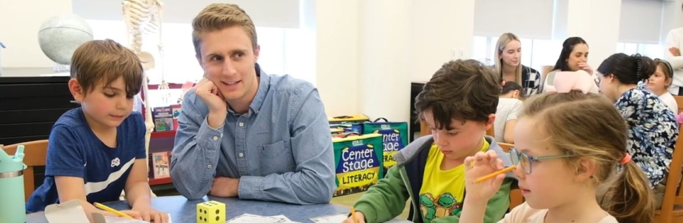 Male graduate students works at a table with three children