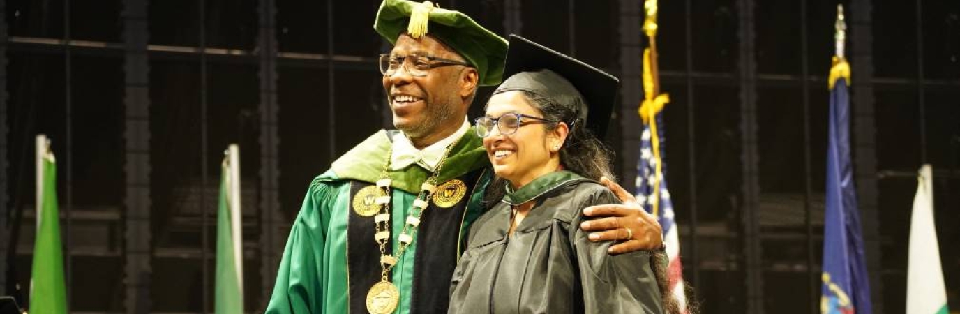 Campus president poses with a graduate with both wearing caps and gowns