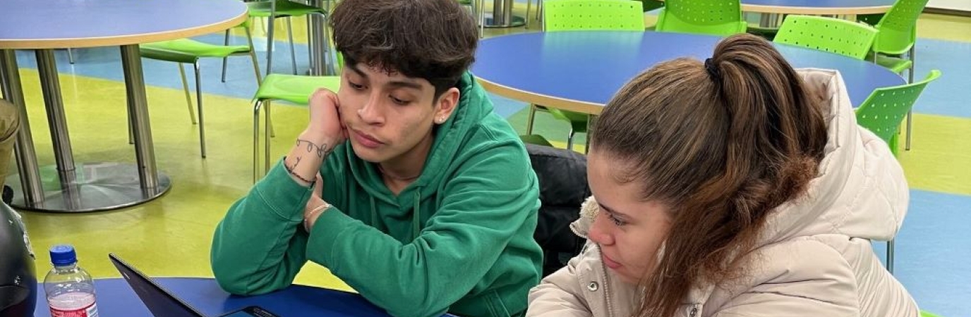 Two students collaborating on a laptop in a classroom.