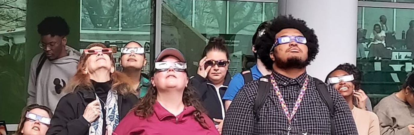 A group of young people wearing eclipse glasses look to the sky