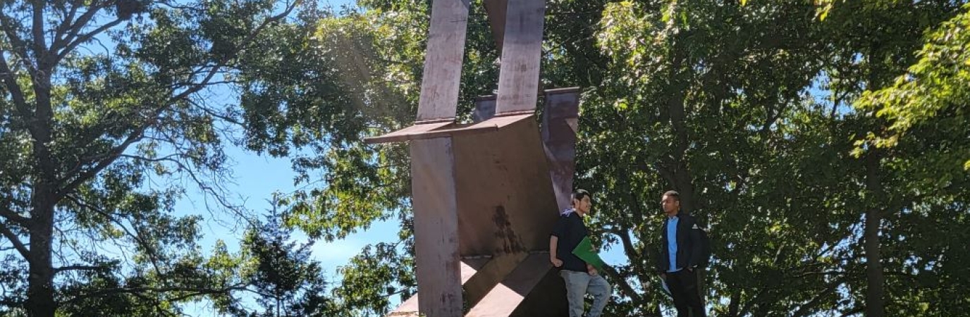 Two male students talk near a sculpture