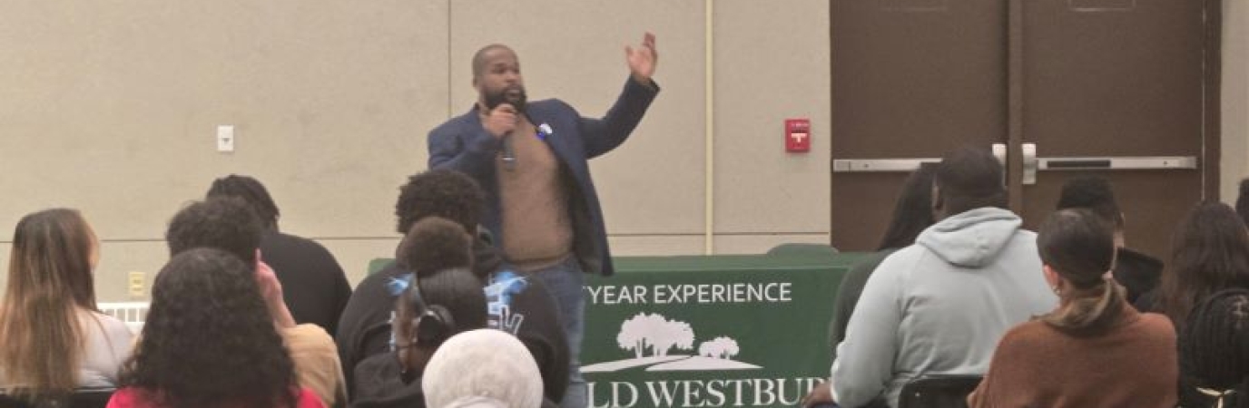 African American man stands and speaks before an audience of young people