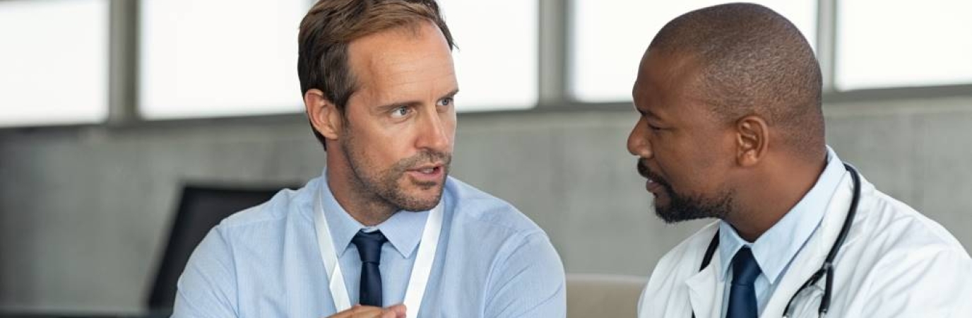 Man in professional dress speaks with man in doctor's garb