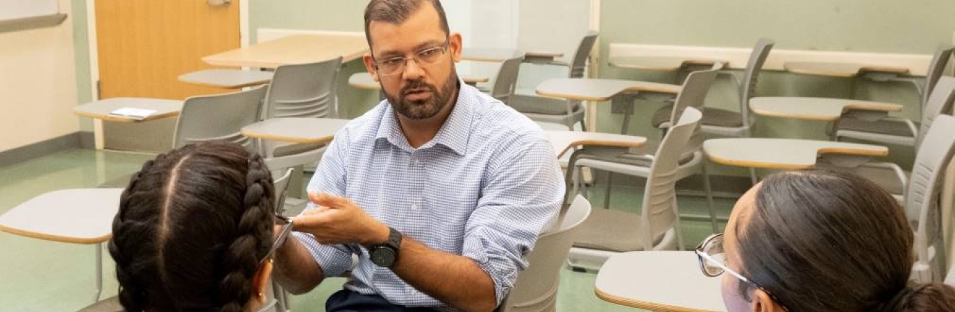 Male professor having discussion with two female, seated students