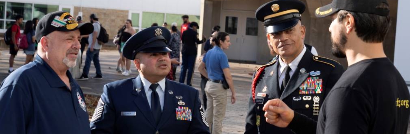 Four men talking, three in military uniforms