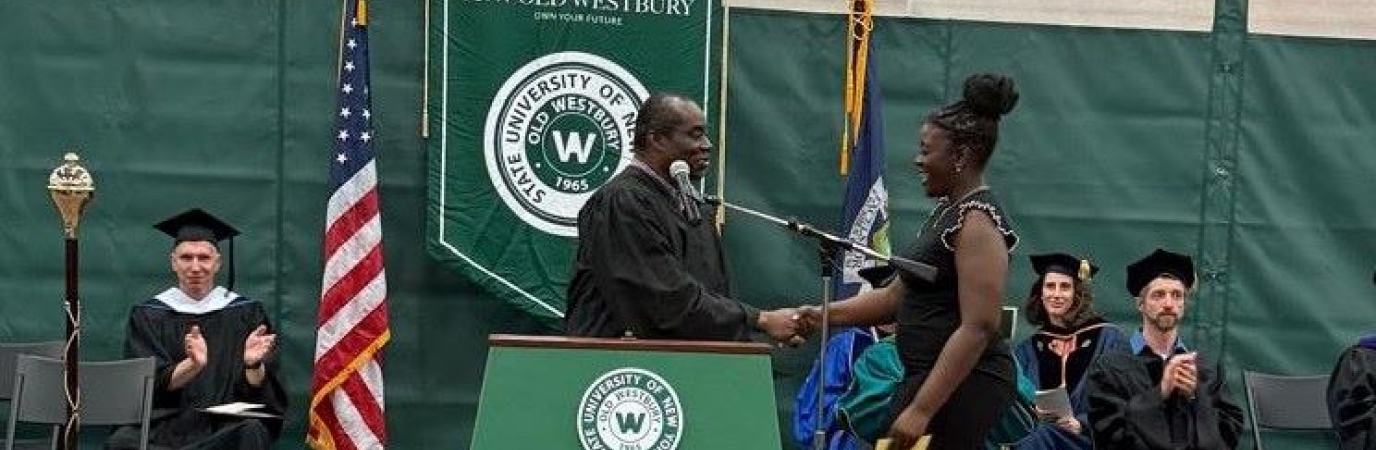Black man dressed in regalia behind a podium shakes the hand of young black woman