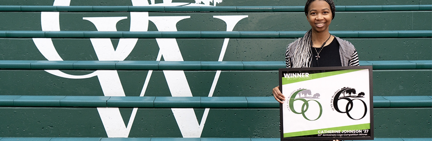 African American young woman stands before a flight of green steps with letters O and W in white while holding a framed print of a logo featuring the number 60