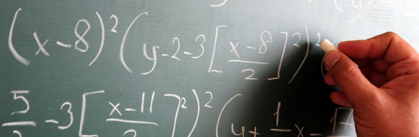 A student hand at a chalkboard covered with math problems