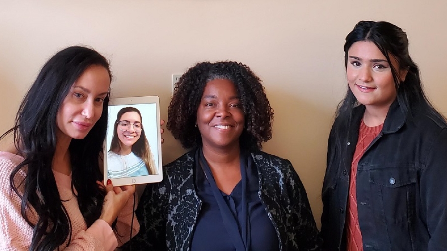 Photo of 3 students - one on a tablet screen - with the Dean of the School of Business