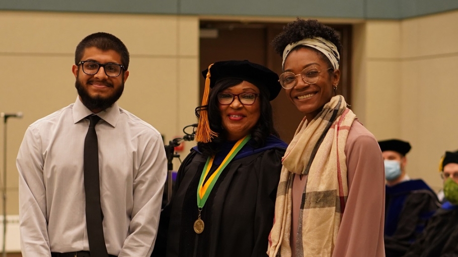 Two students with flanking an administrator in academic regalia
