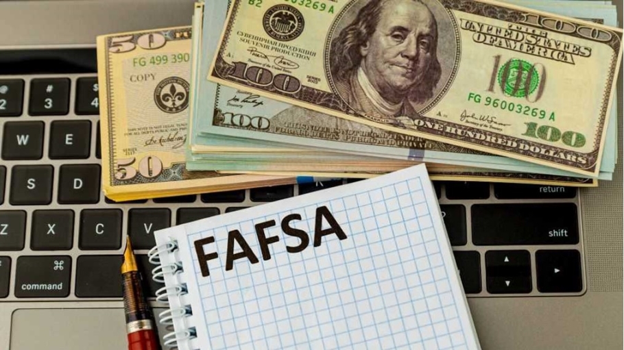 A FAFSA form on top of a keyboard with 100 dollar bills stacked on the keyboard also