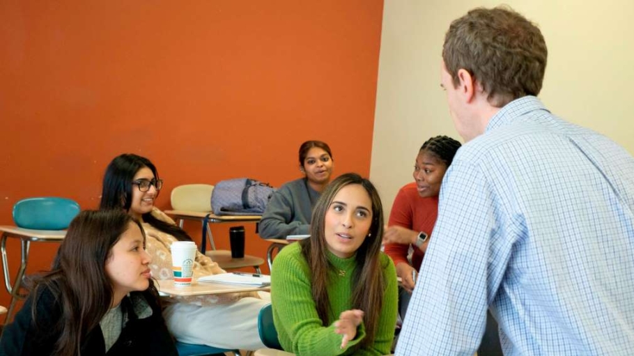 Faculty member standing while speaking with three seated students