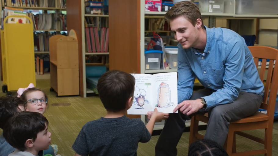Male graduate student reads aloud to four children