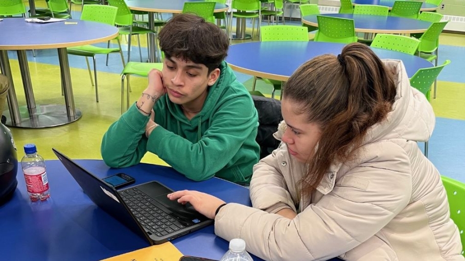 Two students collaborating on a laptop in a classroom.