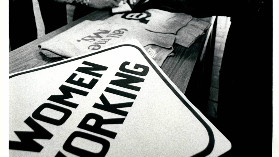 black and white photo of women around table, with sign "women working"