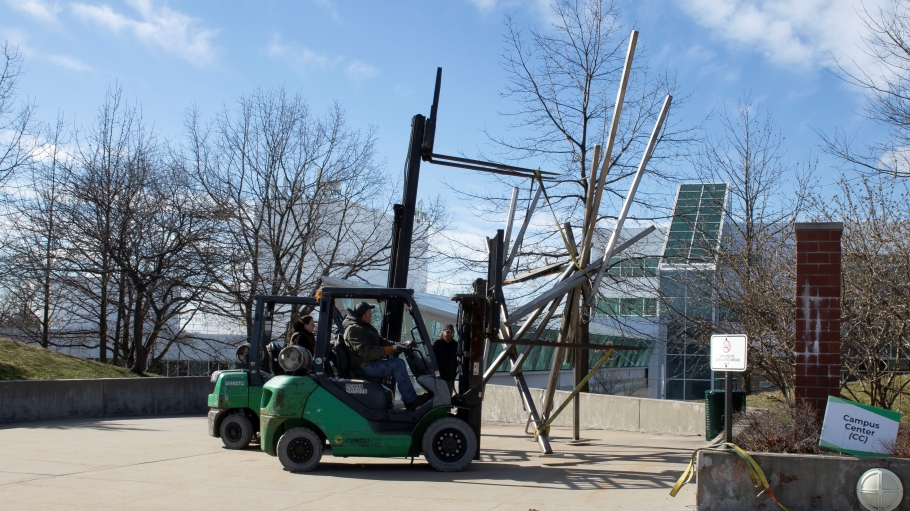 Forklifts raise a metal sculpture from the ground