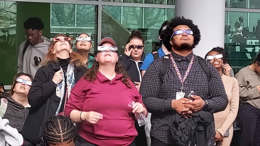 A group of young people wearing eclipse glasses look to the sky