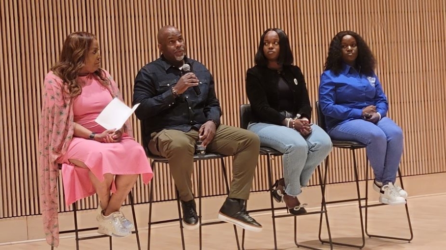 Three African American women and an African American male sit on high stools and hold microphones