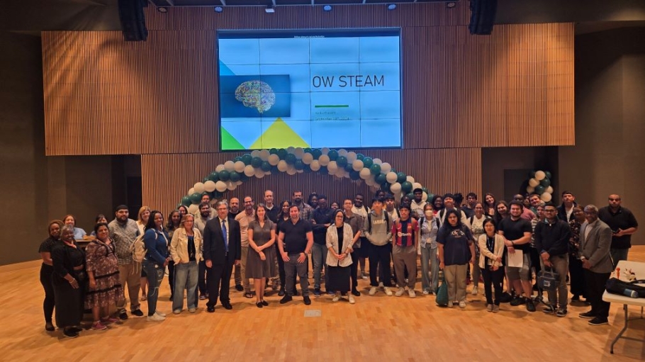 A large group of people from diverse backgrounds pose in an auditorium under a sign that reads OW STEAM