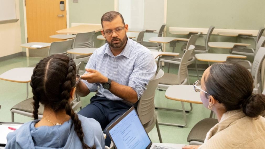 Male professor having discussion with two female, seated students 