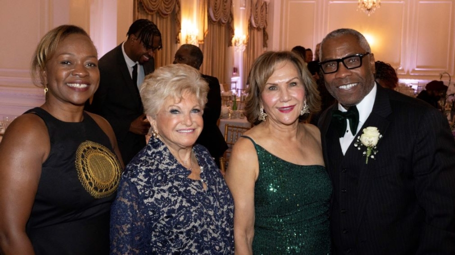 Three women and one man, in formal attire, posing for the photographer