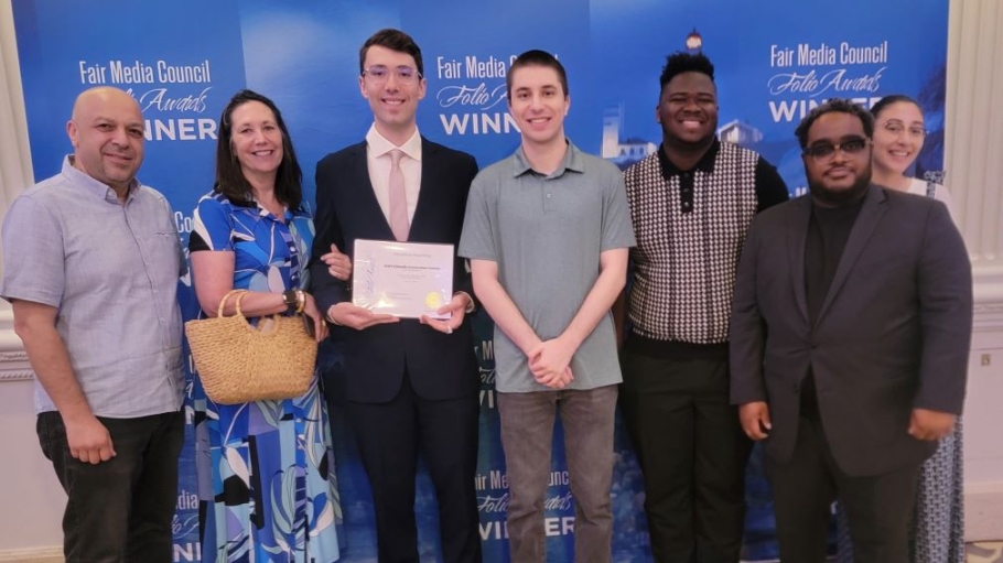 Group of seven men and women with one young man holding an award certificate