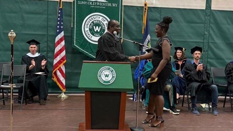 Black man dressed in regalia behind a podium shakes the hand of young black woman